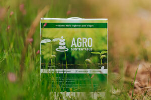 Envase de bioinsumo orgánico de Agro Sustentable (BIOFERT GTG X) en medio de un campo natural, rodeado de hierbas verdes.