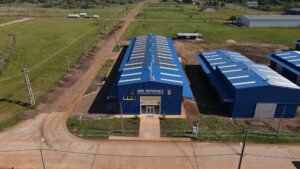 Vista aérea de la planta de Agro Sustentable en Misiones, con techo azul y paneles solares, rodeada de caminos de tierra y áreas verdes.