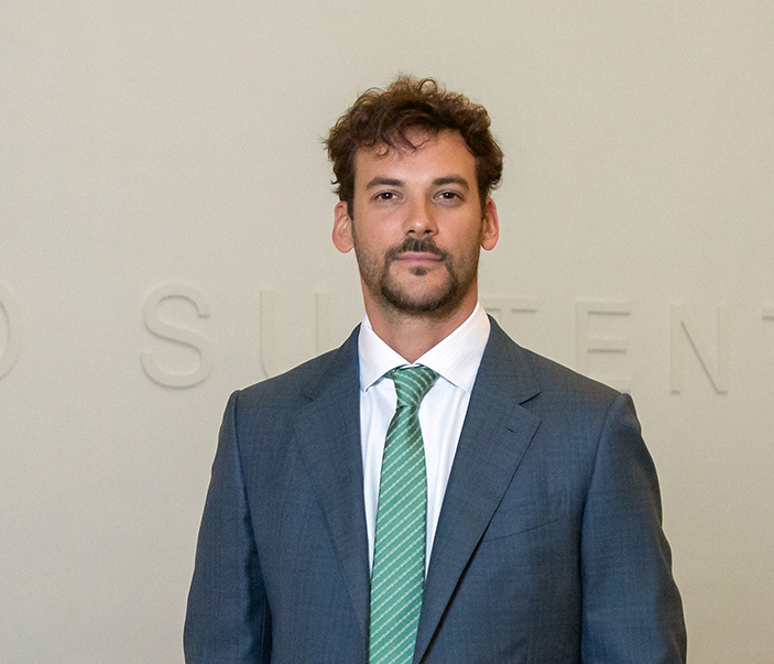 Joaquín Basanta, de traje y corbata, frente a una pared institucional con letras de fondo.